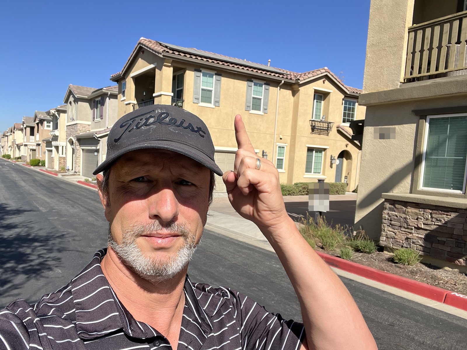 Aaron standing on a residential street, pointing up at a finished rooftop solar array.